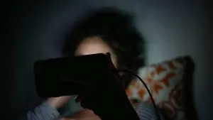 Eine Frau schaut im Bett eine Sendung auf dem Smartphone