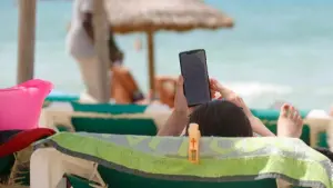 Eine Frau ließt am Strand auf einem Handydisplay einen Text