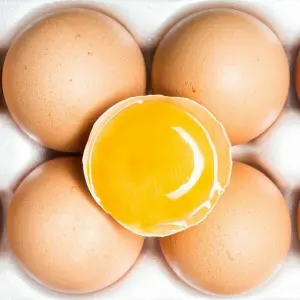 Eine Packung mit Eiern, darauf liegt ein aufgeschlagenes Ei