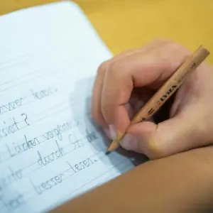 Ein Grundschüler schreibt mit Bleistift in sein Heft