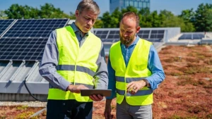 Zwei Arbeiter stehen auf dem begrünten Dach vor einer Solaranlage