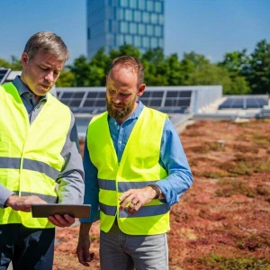 Zwei Arbeiter stehen auf dem begrünten Dach vor einer Solaranlage