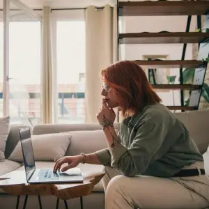 Eine Frau sitzt an einem Laptop auf einer Couch