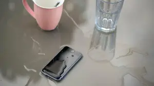 Ein nasses Smartphone neben Tasse und Glas