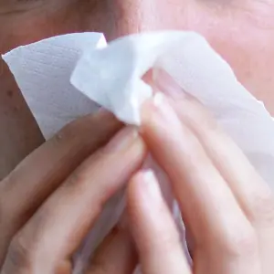 Eine Frau putzt sich die Nase mit einem Papiertaschentuch