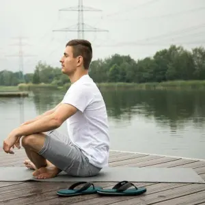 Ein Mann sitzt im Schneidersitz auf einem Steg