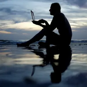 Mann arbeitet am STrand an einem Laptop