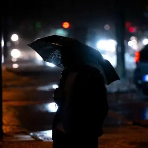 Ein Fußgänger geht in München bei Regen über eine Kreuzung