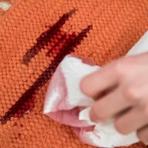 Eine Frau entfernt Rotweinflecken im Teppich mit Küchenkrepp