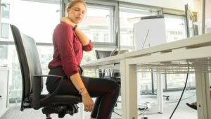 Eine Frau sitzt in einem Büro und hat Nackenschmerzen