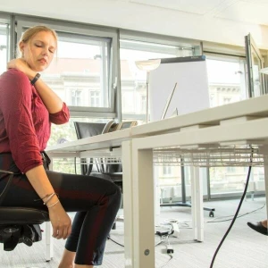 Eine Frau sitzt in einem Büro und hat Nackenschmerzen