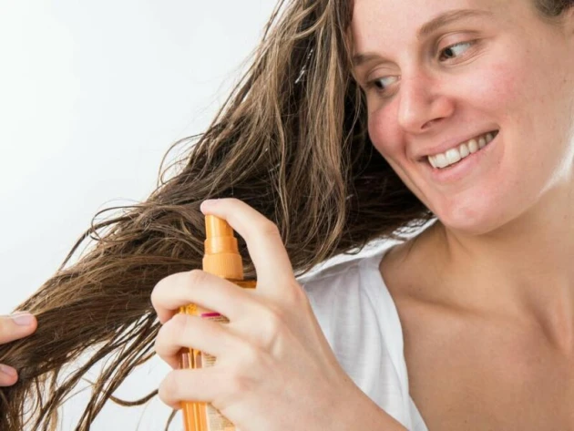 Frau sprüht Haare mit einem Pflegeprodukt ein