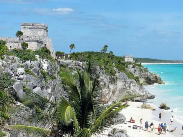 Eine Maya-Ruine und Palmen auf über dem Strand und türkisem Meer.