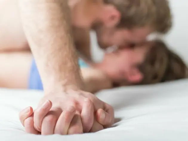 Zwei Menschen im Bett, im Vordergrund verschränkte Hände