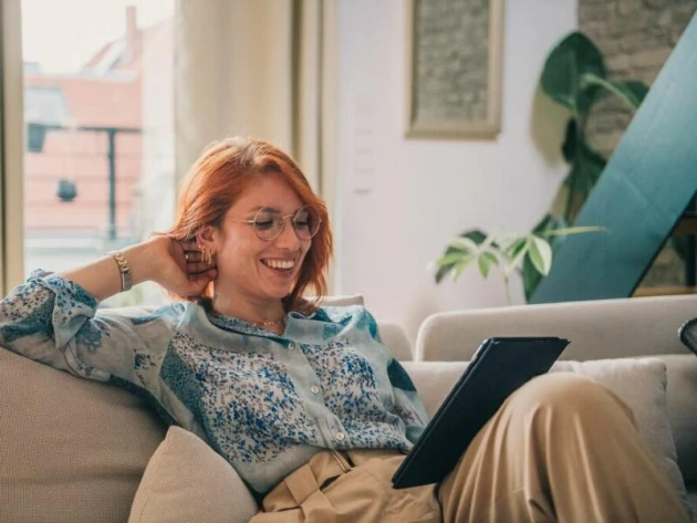 Eine Frau sitzt auf einer Couch und bedient ein Tablet