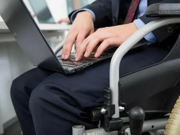 Ein Mann im Rollstuhl arbeitet an Laptop im Büro