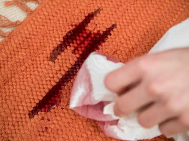 Eine Frau entfernt Rotweinflecken im Teppich mit Küchenkrepp