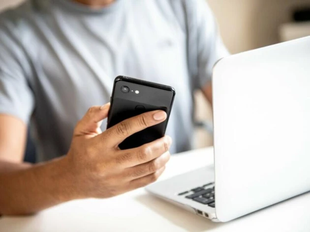 Junger Mann mit Smartphone und Laptop